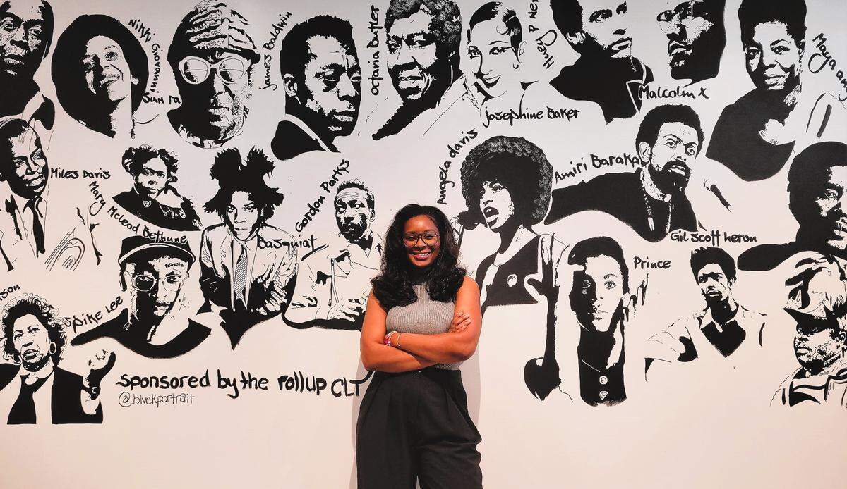Cheryse Terry stands in front of a mural of Black history makers inside Archive.