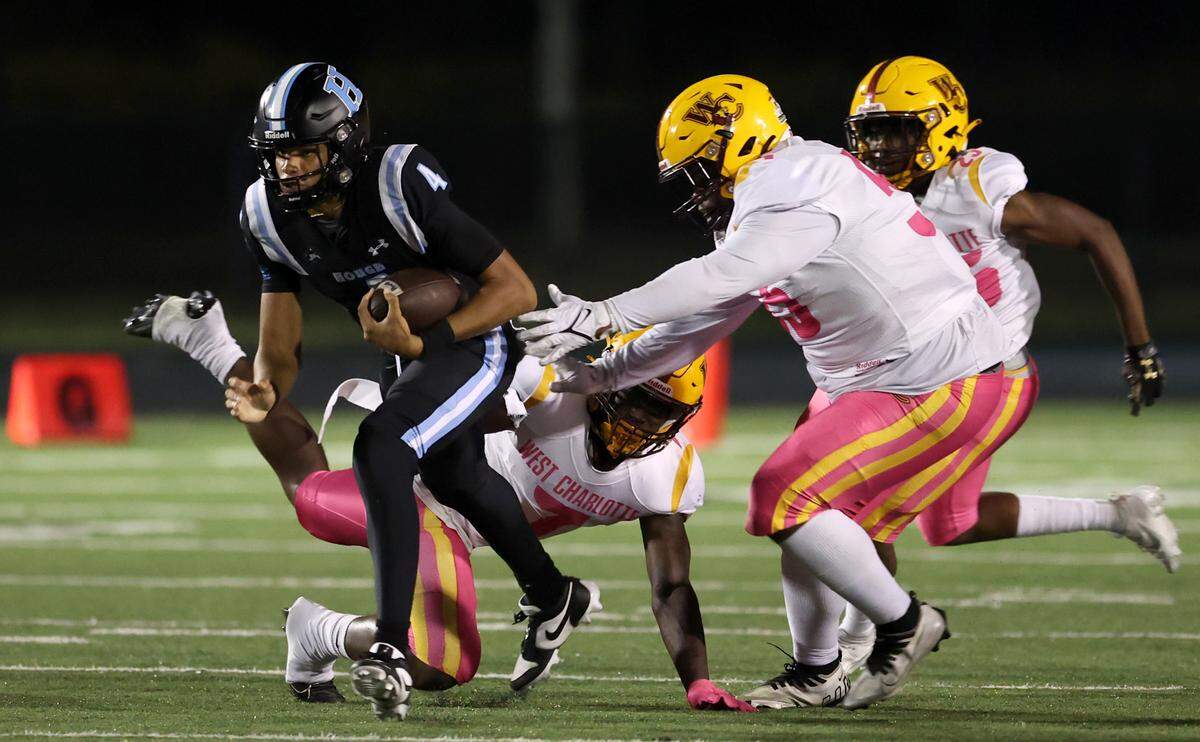 Hough High quarterback Trey Blakeney, left, escapes the grasp of the West Charlotte defense during first half action on Friday, October 6, 2023.