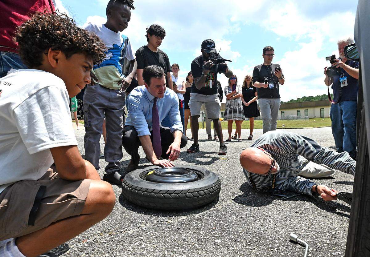 North Carolina Attorney General Jeff Jackson, center, listens to Jason Brown, right, as he teaches students at Dream Center Academy in Gastonia, NC how to change a tire properly on Tuesday.