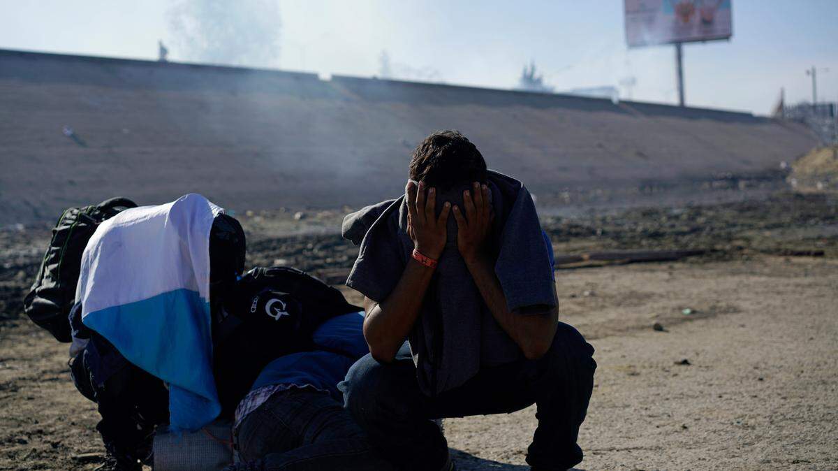 Three Honduran migrants huddle in the riverbank amid tear gas fired by U.S. agents on the Mexico-U.S. border.