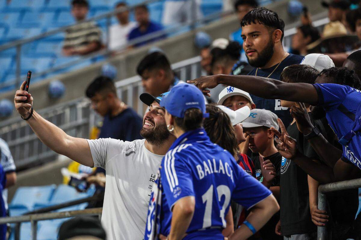 Newly signed Panthers quarterback Baker Mayfield, left, takes a selfie with fans on the sidelines ahead of the match between Charlotte FC and Chelsea FC at Bank of America Stadium on Wednesday.