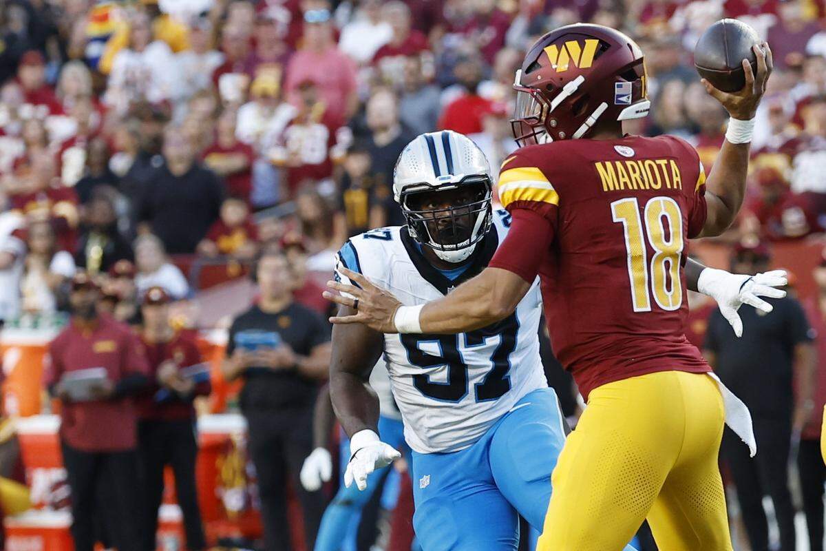 Oct 20, 2024; Landover, Maryland, USA; Washington Commanders quarterback Marcus Mariota (18) passes the ball as Carolina Panthers defensive tackle T.J. Smith (97) chases during the second quarter at Northwest Stadium. Mandatory Credit: Geoff Burke-Imagn Images