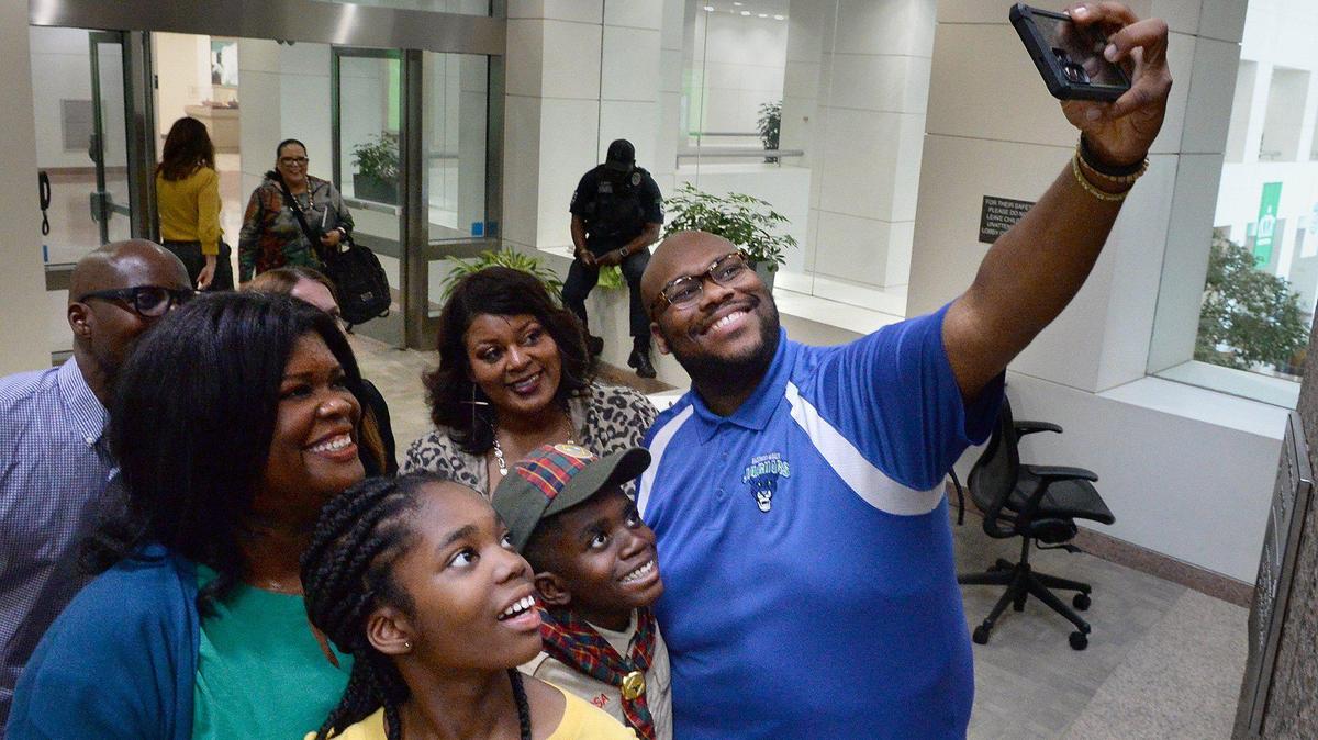 Surrounded by family and staff from Eastway Middle School, Ayahn Ambroise, 12, (bottom left in yellow) joins in for a congratulatory photo after leading the Pledge of Allegiance at the CMS board meeting April 4.