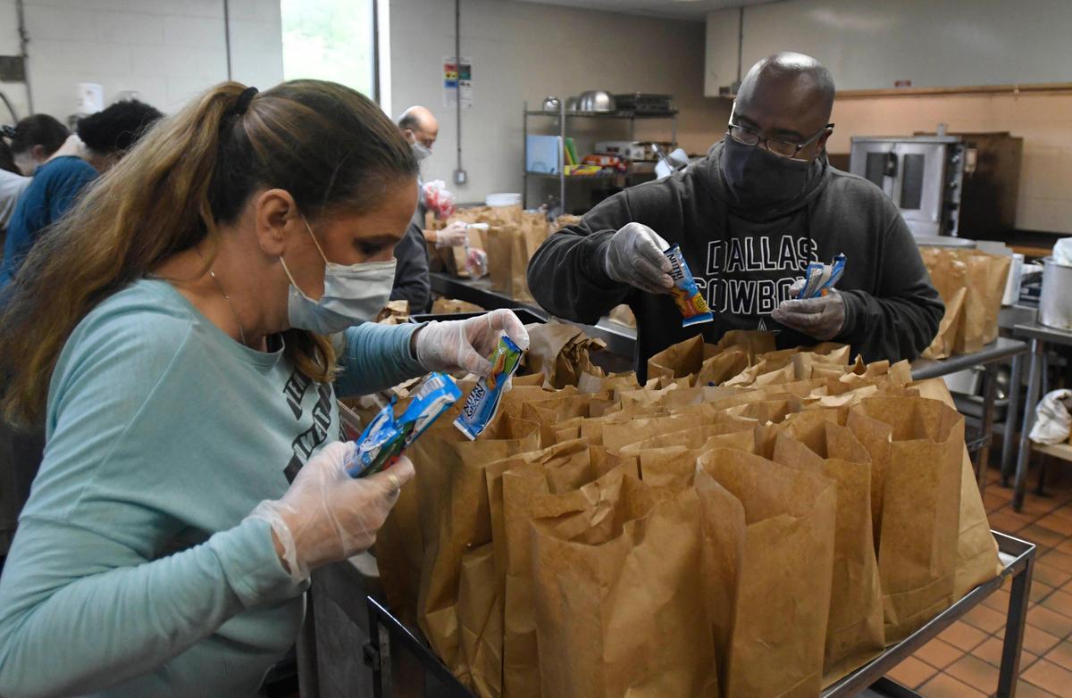 Charles Robinson, right, helps volunteer Diana McKenzie, left, to fill lunch bags for children in the kitchen of Northside Baptist Church on Monday, April 20, 2020.