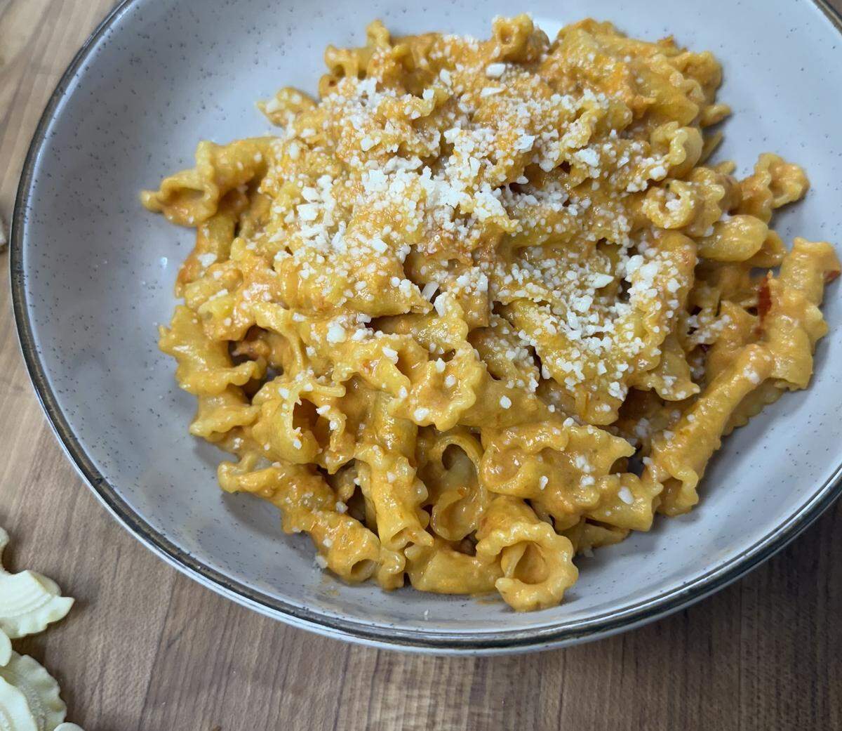 A close-up of a white bowl filled with mafaldine pasta tossed in a creamy orange sauce and topped with grated Parmesan cheese.