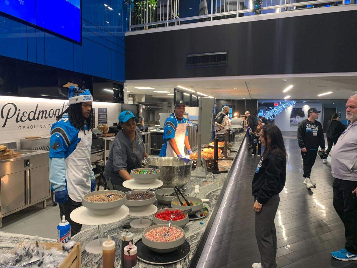 Panthers owner Nicole Tepper greets running backs Jonathon Brooks (left) and Chuba Hubbard (right) as they volunteer at the sixth annual “Joy to the Carolinas” event at Bank of America Stadium on Tuesday, Dec. 17, 2024.