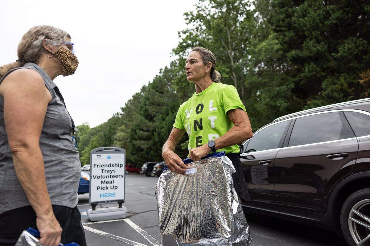 Kelly Bass, left, hands Dee Kantner a Friendship Trays delivery bag at Loaves & Fishes and Friendship Trays in Charlotte, N.C., on Wednesday, June 8, 2022.