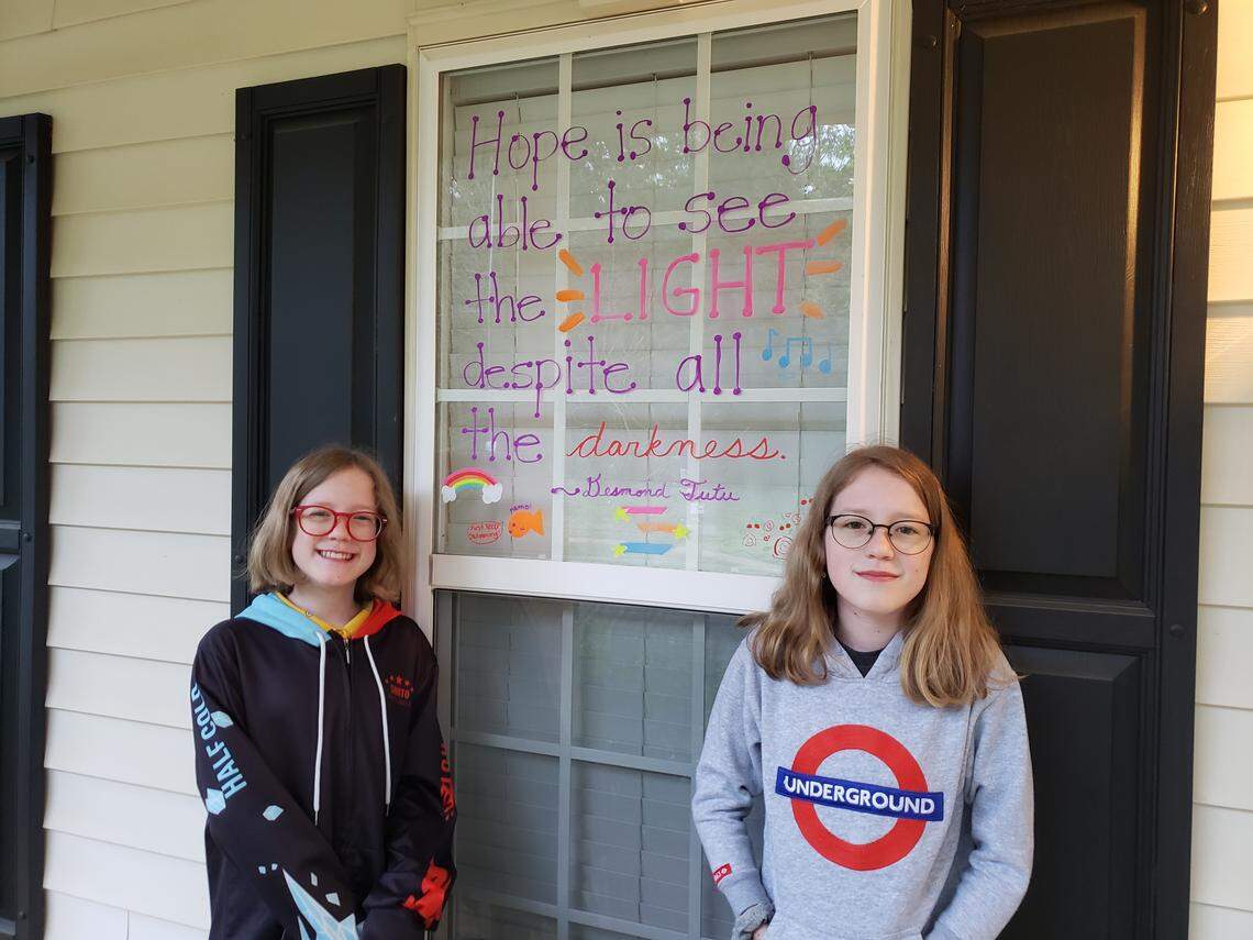 The Nichols family has also starting writing messages in their window to inspire their community during the coronavirus pandemic. Twin sisters Tessa and Savannah, 12, pose with their latest note.