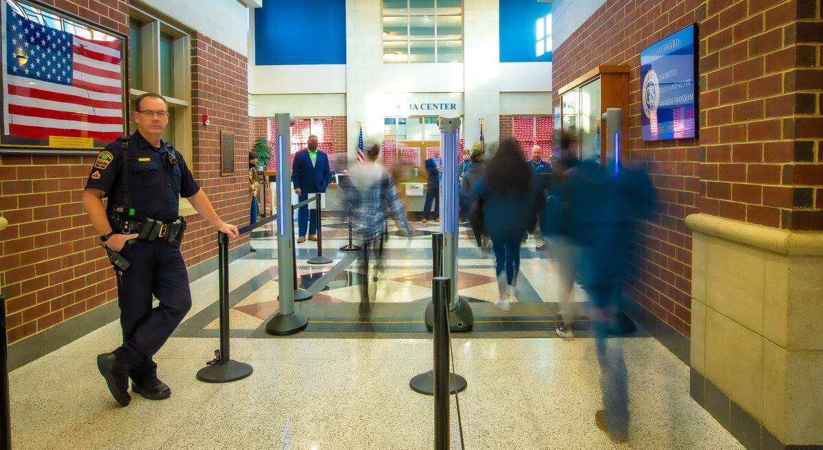 A police officer watches as students walk through body scanners at Dorman High School in Spartanburg, South Carolina. CMS officials consulted the Spartanburg district before implementing their own scanners.
