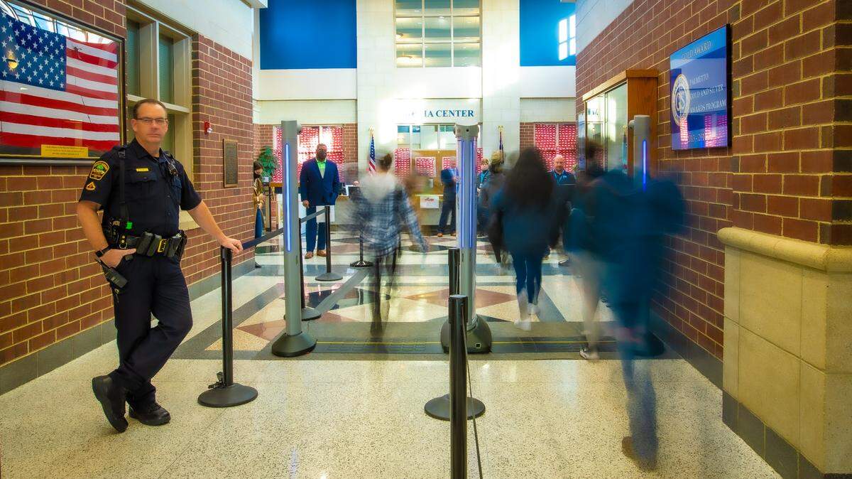 A police officer watches as students walk through body scanners at Dorman High School in Spartanburg, South Carolina. CMS officials consulted the Spartanburg district before implementing their own scanners.
