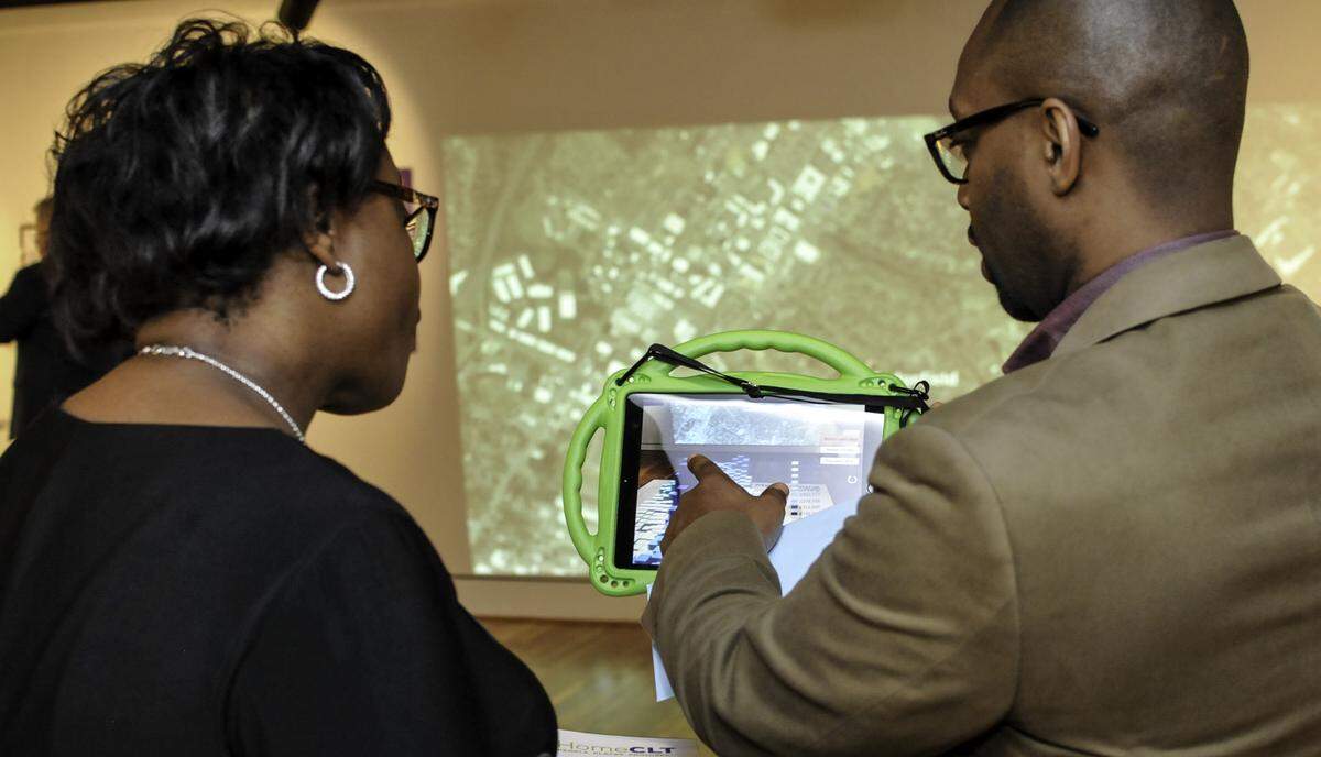 Levine Museum historian Willie Griffin (right) explains the augmented reality piece of the #HomeCLT exhibit to a museum patron during the opening reception.