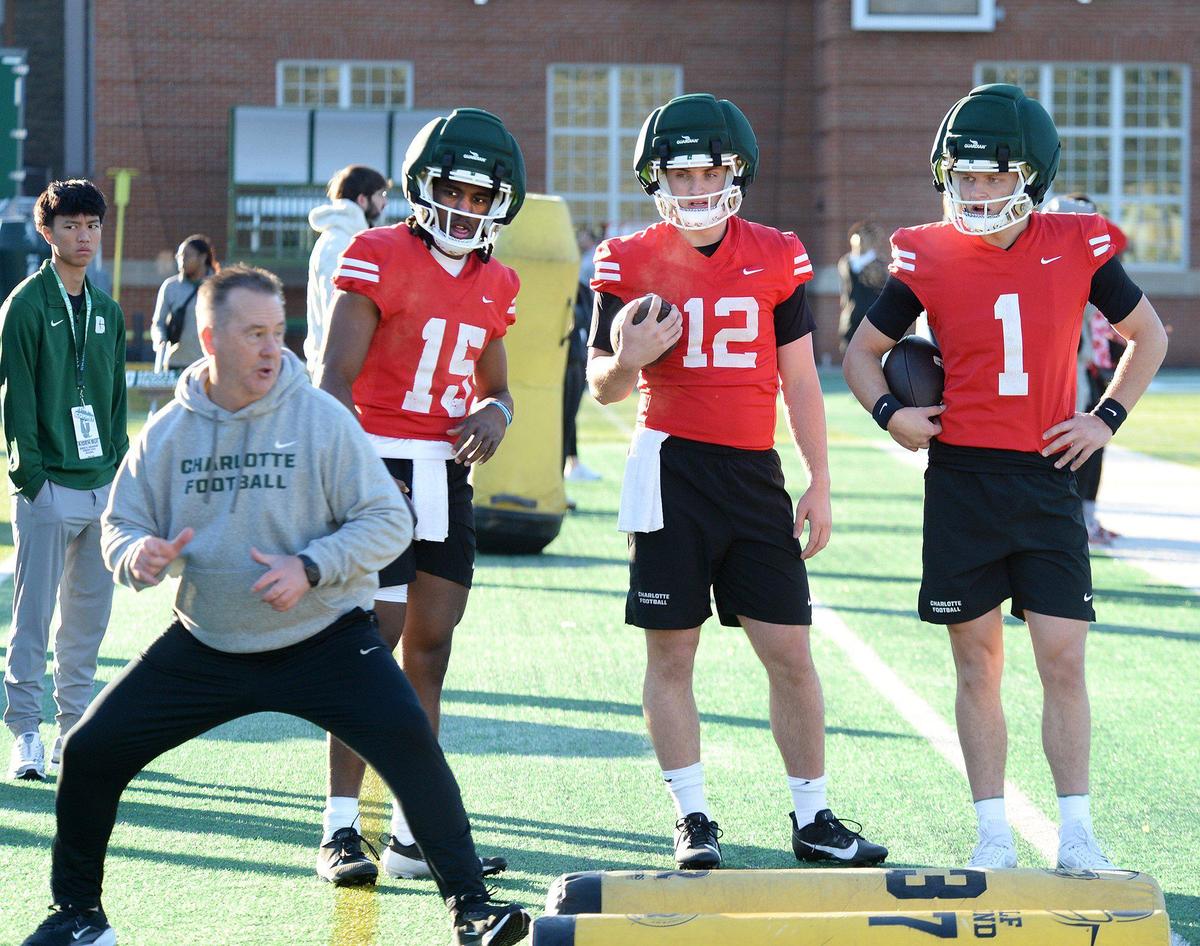 Todd Fitch, Charlotte 49ers associate head coach, demonstrates a drill for quarterback #15,Conner Harrell, #12, Grayson Loftis, and #1, Zach Wilcke, during an open practice at the university on Tuesday, Mar. 18, 2025.