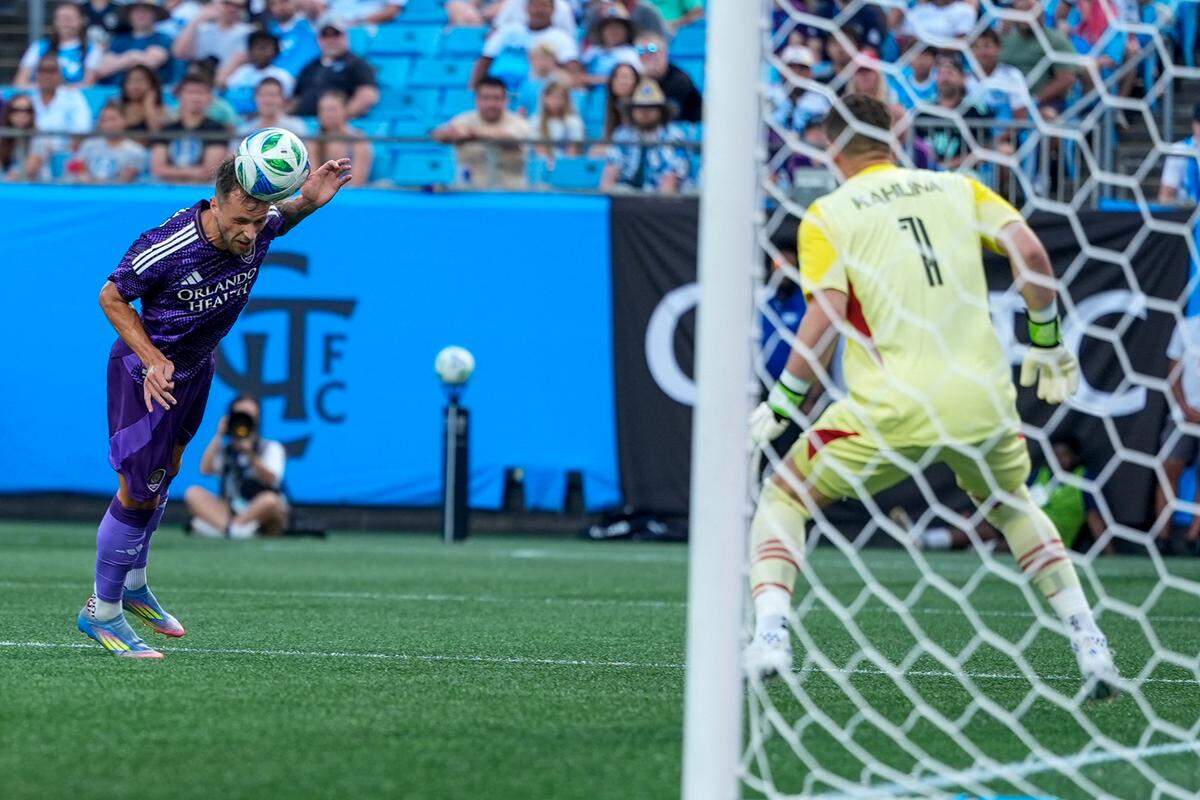 Jul 5, 2025; Charlotte, North Carolina, USA; Orlando City midfielder Martin Ojeda (10) heads the ball at the goal as Charlotte FC goalkeeper Kristijan Kahlina (1) looks on during the first half at Bank of America Stadium. Mandatory Credit: Jim Dedmon-Imagn Images