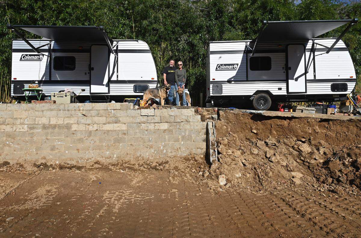 John Grinstead, left, and his wife, Lisa Cooper, right, stand with their dogs Luna and Moe near the foundation of their basement in Burnsville on Monday, Nov. 25. The couple’s home along with John’s father’s home were destroyed by Hurricane Helene in September. The couple are now living in campers supplied by Operation Helo.