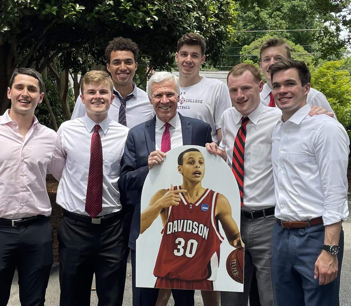 Seven members of Davidson’s Class of 2022, along with head coach Bob McKillop (in suit jacket, holding cutout of Steph Curry), celebrated the school’s graduation on May 15, 2022. Curry’s graduation came 13 years after he left college a year early for the NBA in 2009. Left to right, front row: manager Sourna Daneshvar, player Drew Dibble, McKillop, manager Joe Nero, player Ben Craig. Second row, L-R: players Nelson Boachie-Yiadom, Luka Brajkovic and Michael Jones.