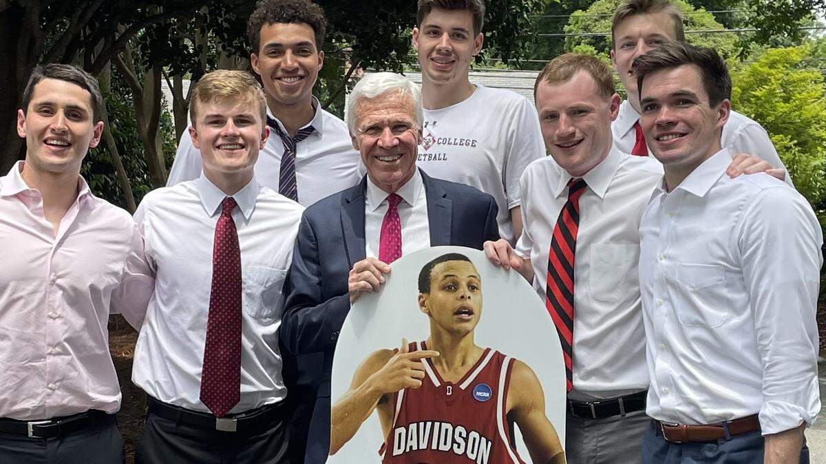 Seven members of Davidson’s Class of 2022, along with head coach Bob McKillop (in suit jacket, holding cutout of Steph Curry), celebrated the school’s graduation on May 15, 2022. Curry’s graduation came 13 years after he left college a year early for the NBA in 2009. Left to right, front row: manager Sourna Daneshvar, player Drew Dibble, McKillop, manager Joe Nero, player Ben Craig. Second row, L-R: players Nelson Boachie-Yiadom, Luka Brajkovic and Michael Jones.