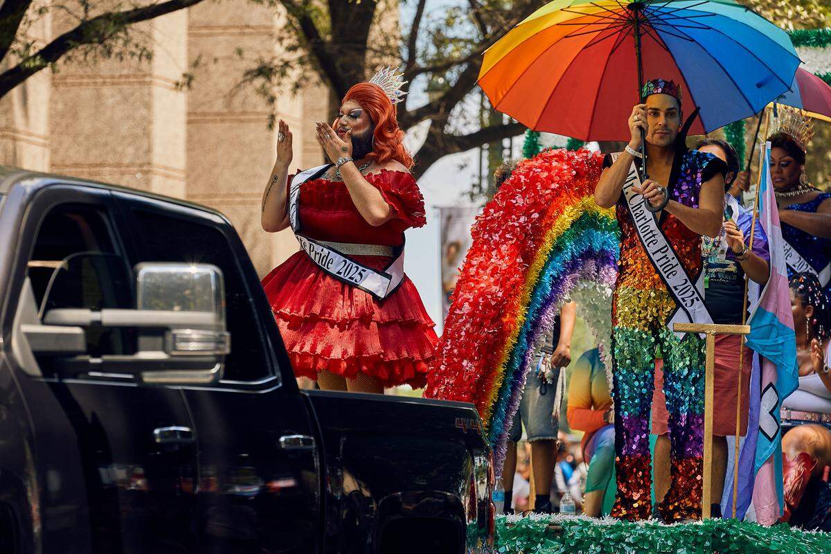 Mx. Charlotte Pride & Mr. Charlotte Pride look onto the crowd and wave as their float passes down North Tyron Street during the 25th Charlotte Pride Parade in uptown Charlotte on August 17, 2025.