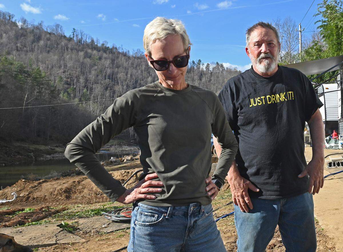 Lisa Cooper, left, and her husband, John Grinstead, right, stand near their former home in Burnsville, N.C., on Monday, Nov. 25. The couple’s home along with John’s father’s home were destroyed by Hurricane Helene in September. The couple are now living in campers supplied by Operation Helo.