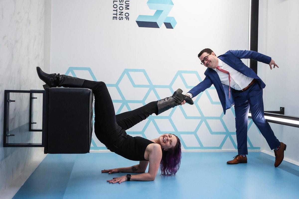 Mel Fox, left, and Jason Thomas pose in the reverse room, that gives the appearance of defying gravity, at the grand opening ceremony for Museum of Illusions Charlotte on Tuesday. The Charlotte location is the 39th museum, across 25 countries. The public will be able to visit starting Friday, Dec. 9.