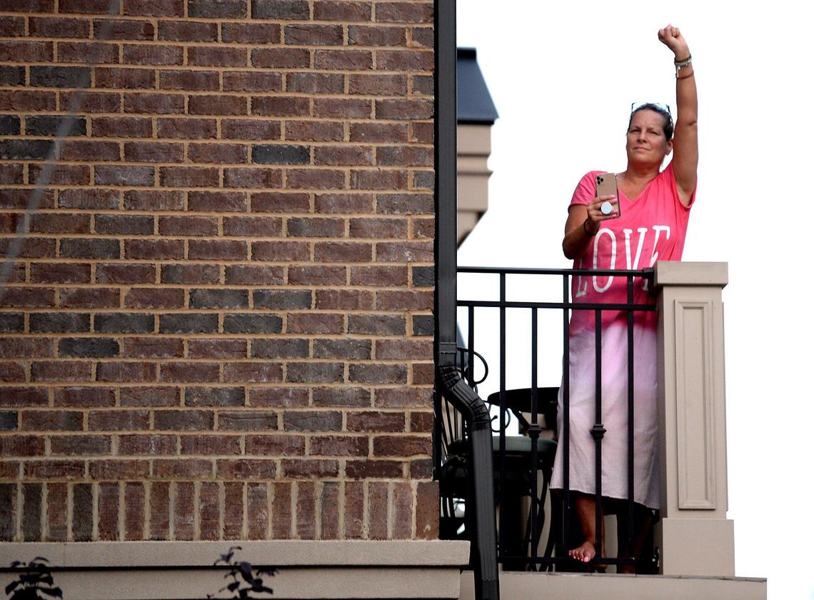 A woman stands on the balcony of her townhouse with her fist raised in support of demonstrators on Friday, June 5, 2020. Demonstrators have been marching throughout Charlotte for eight days in response to the killing of George Floyd, a black man who was killed on Monday, May 25, 2020 by a Minneapolis, MN police officer.