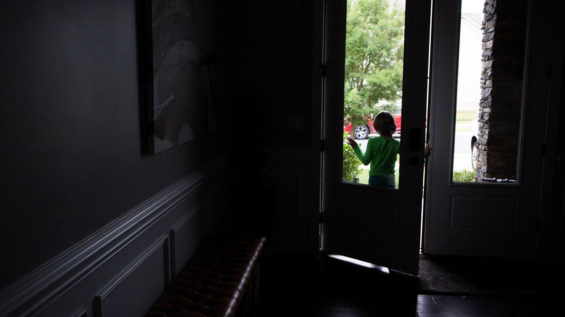 After playing outside, a child stands in the doorway of their Charlotte foster home before heading inside.