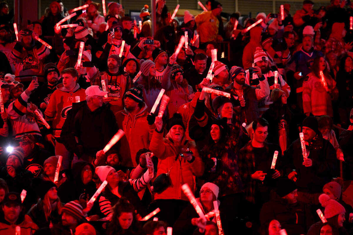 Fans are illuminated by red glow sticks as they prepare to watch the Charlotte Checkers battle the Rochester Americans during the 2024 Queen City Outdoor Classic at Truist Field in uptown Charlotte, NC on Saturday, January 13, 2024.