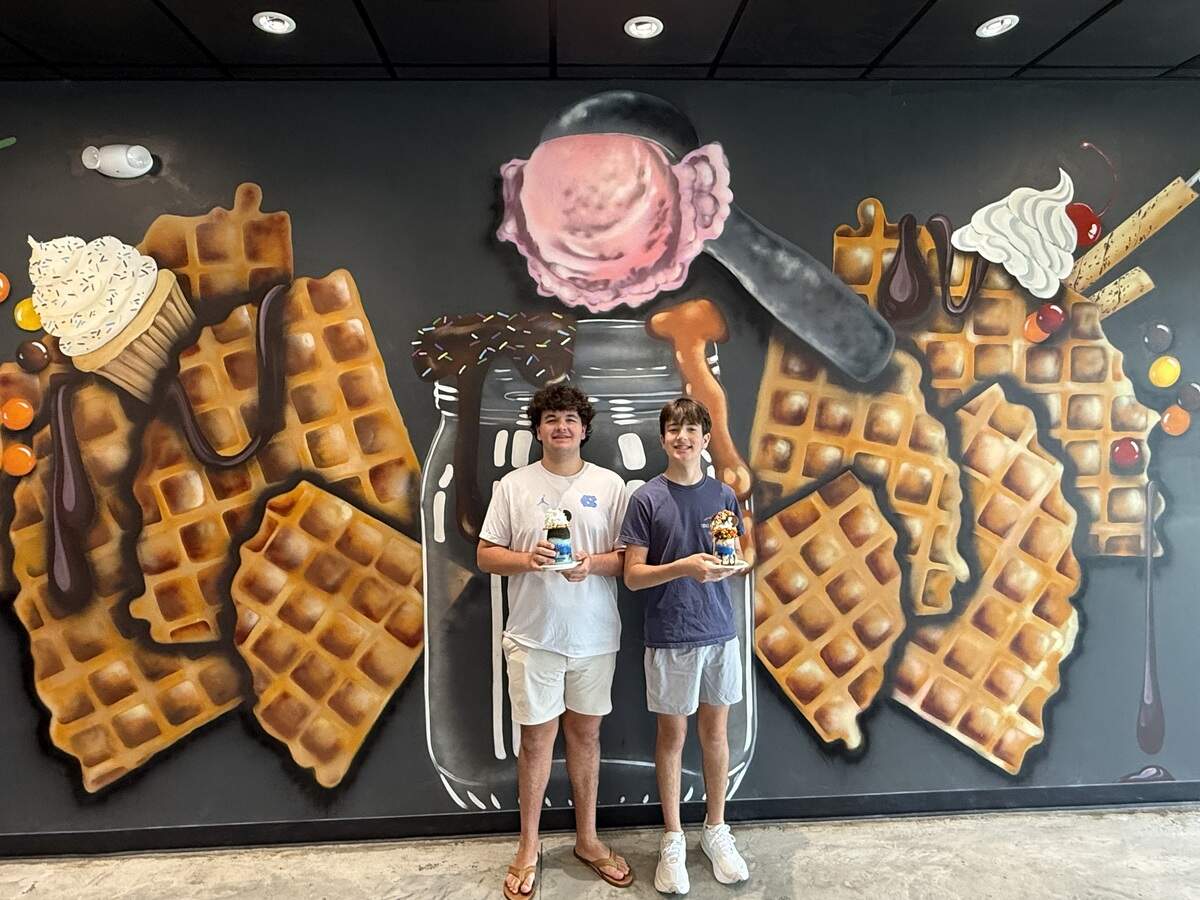 Two teenagers holding milkshakes while standing in front of a large painted wall mural depicting giant waffles and ice cream.