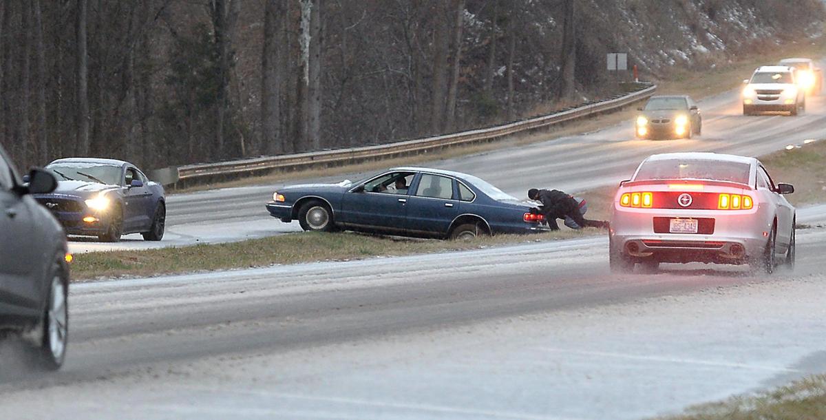 Men try to push a car from the median along Independence Boulevard on Sunday as snow and sleet blanket the roadway. 