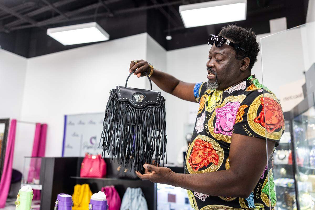 J Winston Roberts, owner of Privee Clothing at Queen City Quarter, shows off designer handbags in his store. He said business is building since opening in 2023. But he still needs to increase awareness of the shop.