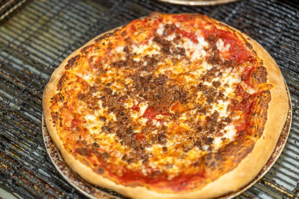 A freshly baked pizza with a thick crust, topped with tomato sauce, melted cheese, and ground sausage. It is on a round metal pan sitting on a wire rack.