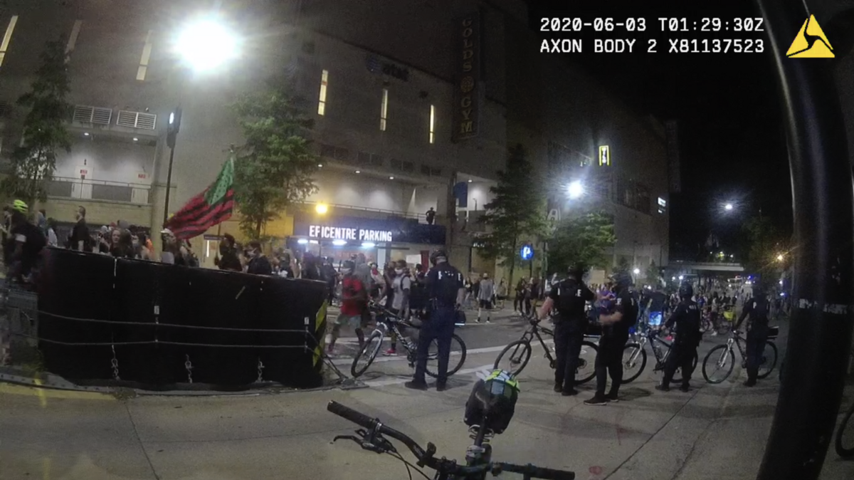 Screen shot from body worn camera shows row of police officers while protesters walk past. Protesters march and chant after the killing of George Floyd by the hands of police officers. 