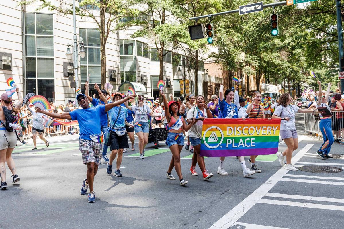 Parade participants march and cheer while holding a Discovery Palace banner during the Charlotte Pride Festival & Parade on Sunday, Aug. 18, 2024