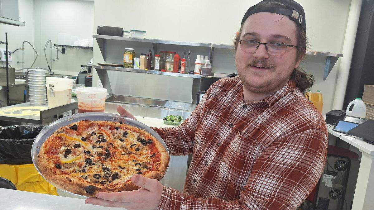 Nate Pillow, general manager of Mamma Ramona’s Pizzeria in downtown Mooresville, holds a fresh-out-of-the-oven Veggie Deluxe 14-inch pizza on Thursday, Feb. 13, 2025.