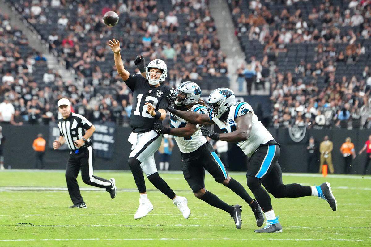 Las Vegas Raiders quarterback Aidan O’Connell (12) makes a touchdown pass under pressure from Carolina Panthers linebacker Shaq Thompson (54) and Carolina Panthers defensive end A’Shawn Robinson (94) during the fourth quarter at Allegiant Stadium.
