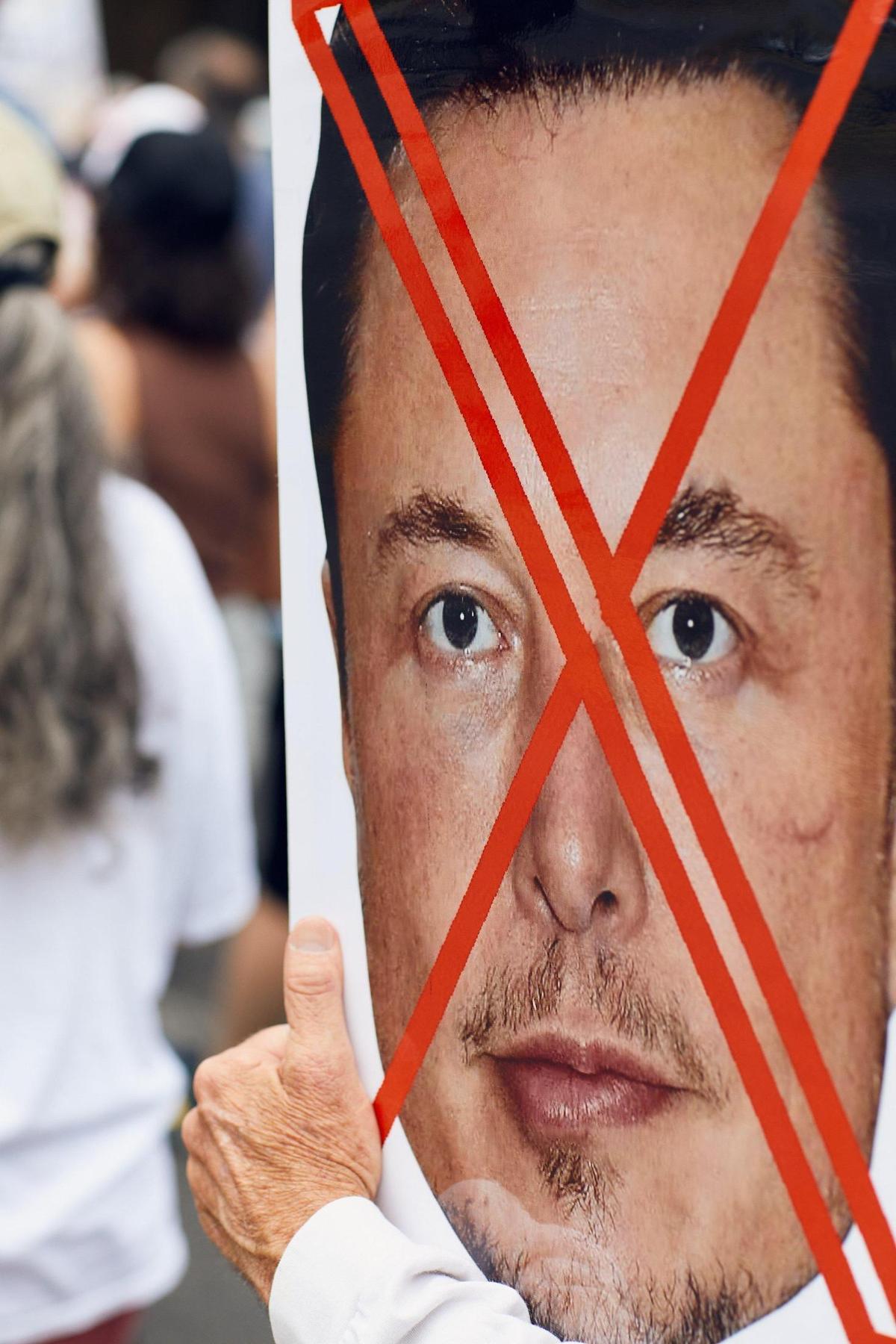 A man carries a sign with a crossed out Elon Musk face at an anti-Trump protest in Charlotte Saturday.