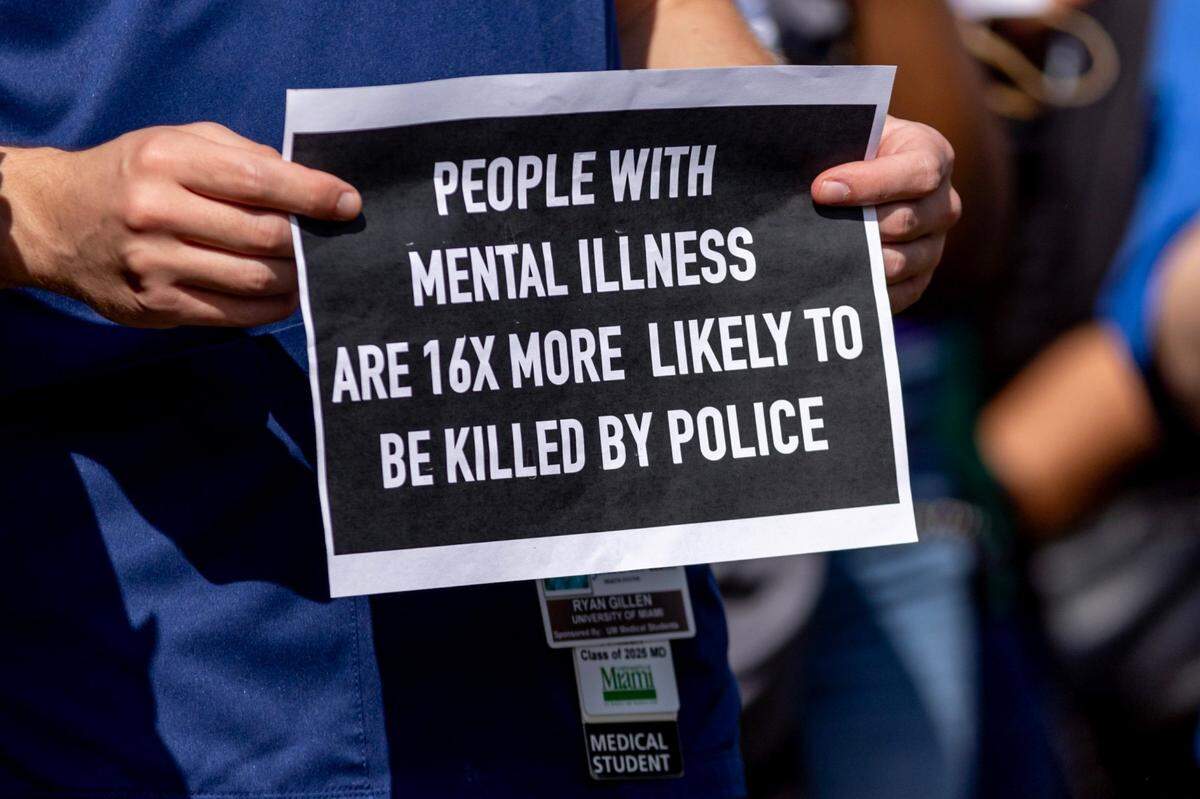University of Miami Medical Student Ryan Gillen holds a sign that reads “People With Mental Illness Are 16x More Likely To Be Killed By Police” during a March 14 press conference held by the Healing and Justice Center across the street from the scene of the shooting in Florida. Miami police shot Donald Armstrong more than five times while responding to an emergency call during a mental health crisis.