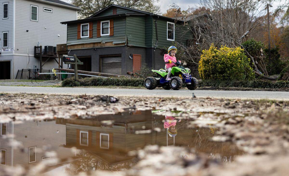 Jojo Fennel rides her toy 4-wheeler past Missy Hubbard’s vacant, flood-damaged house on Riverside Drive in Charlotte last November.