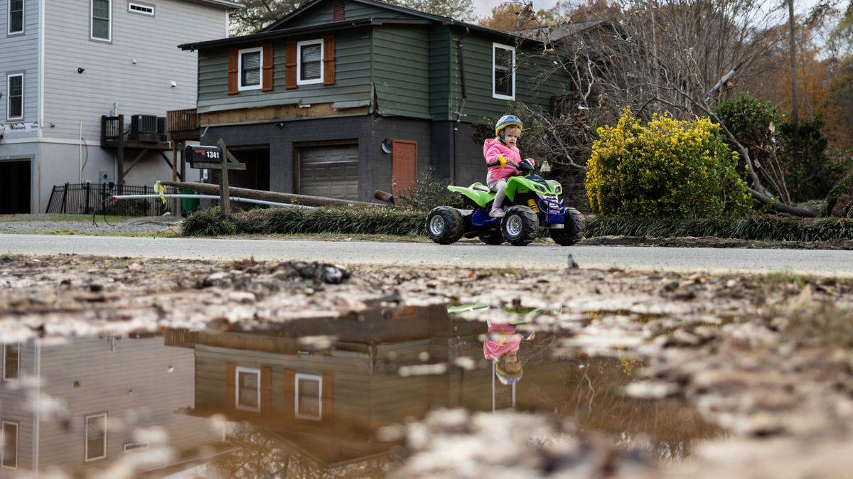 Jojo Fennel rides her toy 4-wheeler past a vacant, flood-damaged house on Riverside Drive in Charlotte last November.