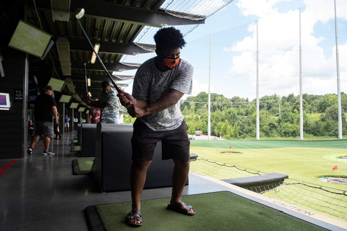 Ian Jefferson, 21, of Charlotte, wears a mask while keeps his eye on the ball during his back swing at TopGolf, Monday, August 3, 2020. As a result of the coronavirus pandemic, TopGolf’s reopening policies require guests to wear masks in common areas, but they can be removed when outdoors if desired.