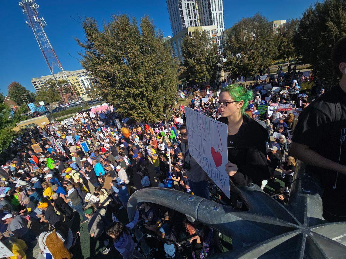 A protester holds a sign that reads “Migrants are the heart of this country” during the No Kings rally in First Ward Park on Saturday, Oct. 18, in Charlotte.