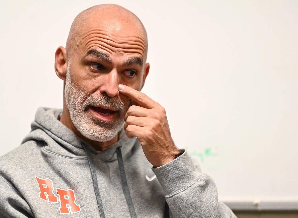 Rocky River head football coach Kenneth McClamrock wipes his eye as he discusses defensive back Elijah Phillips moving into the family's home during the past football season.
