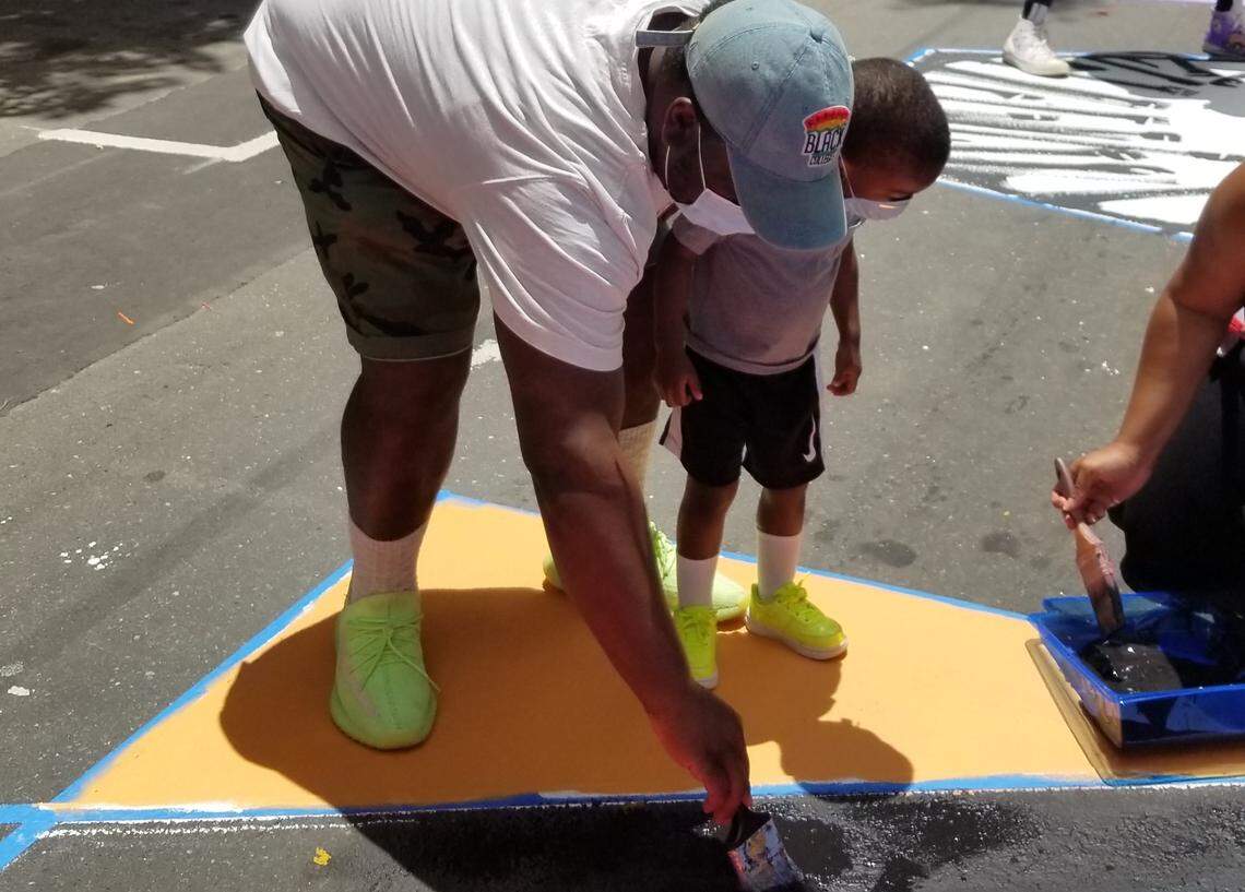 Winston Robinson with his 3-year-old son, Blake, painting the ‘M’ in the Black Lives Matter mural.
