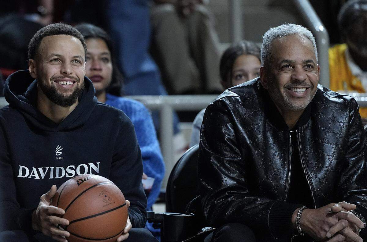 Golden State Warrior guard and Davidson alumni Stephen Curry, left, sits next to his father Dell Curry during the first half of an NCAA college basketball game between Davidson and Duquesne, Tuesday, Dec. 30, 2025, in Davidson, N.C.