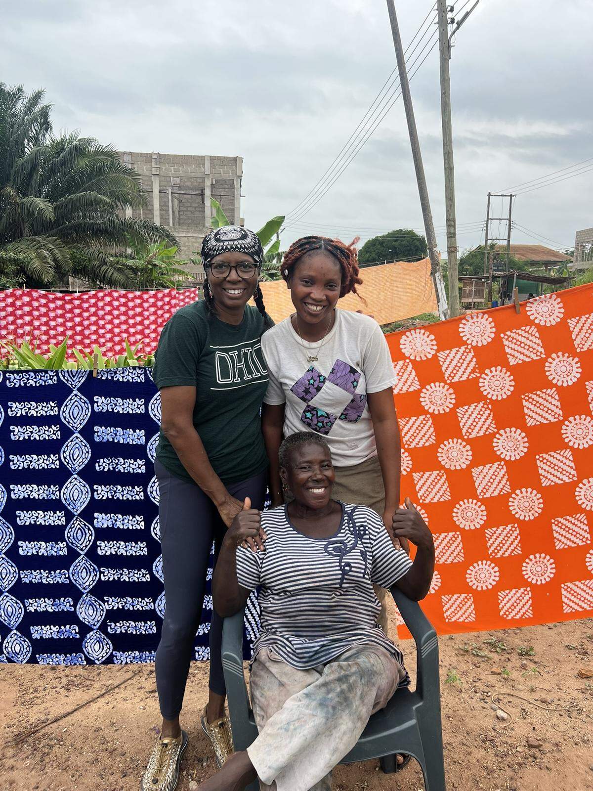 Charlotte artist Lydia Thompson, left, spent a day working with batik artist “Auntie Matta,” seated, and her assistant, Elizabeth, on her recent trip to Ghana. Designs created by Thompson, in collaboration with the other women, hang behind them.
