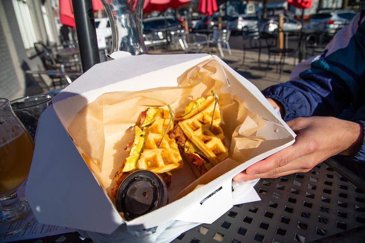 Heist Brewery’s Chicken and Waffle Sandwich includes bacon, eggs and a side of maple syrup to compliment its spicy fried chicken.