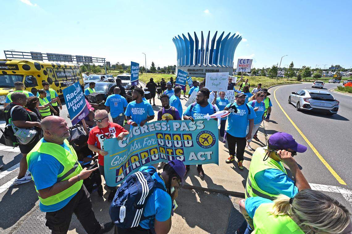 The entrance to Charlotte Douglas International Airport serves as the backdrop as workers stand Tuesday on a median while marching in protest for a living wage, better working conditions and benefits to be including in the FAA Regulation bill.