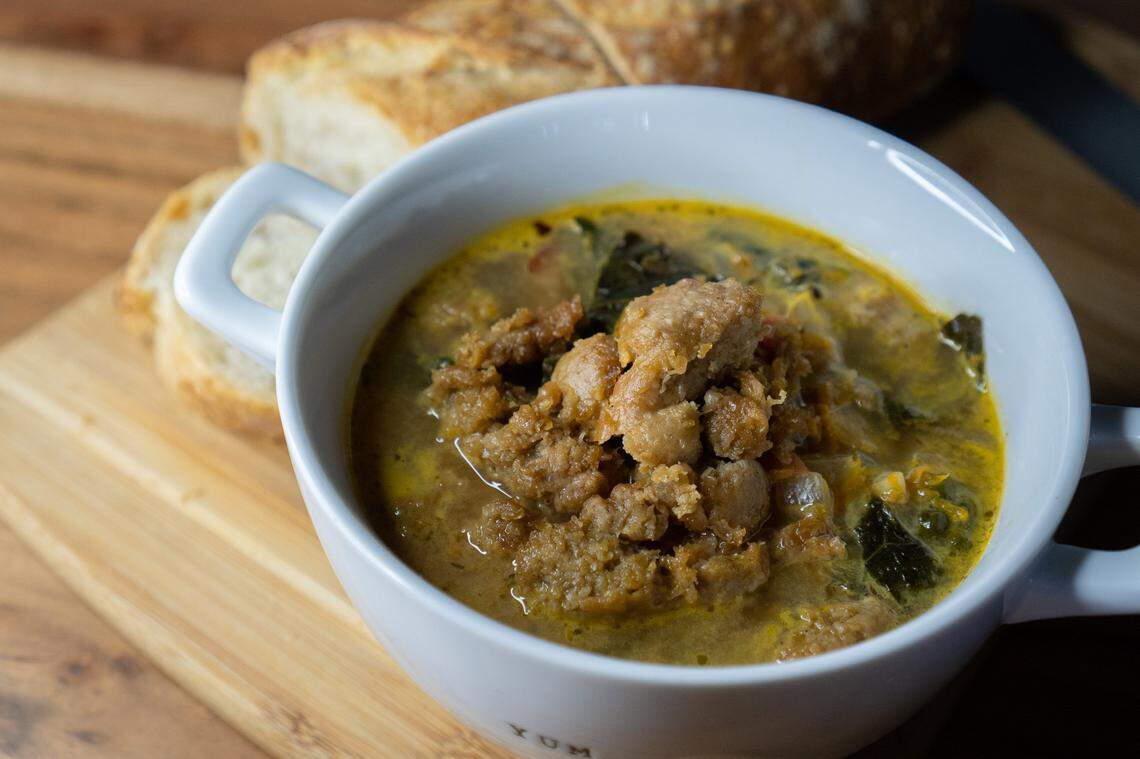 Italian Wedding Soup in a bowl in front of sliced bread.
