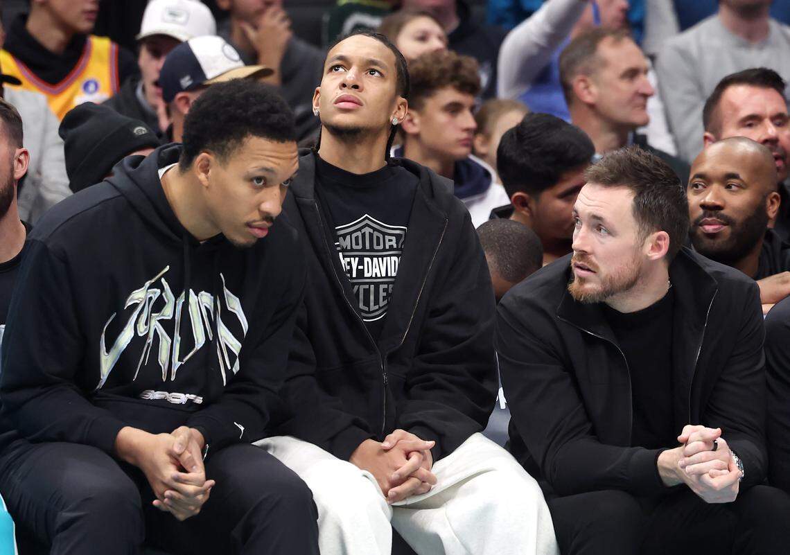 Injured Charlotte Hornets forward Grant Williams, left, guards Tre Mann, center and Pat Connaughton, right, sit on the team’s bench during action against the Denver Nuggets at Spectrum Center in Charlotte, NC on Sunday, December 7, 2025.