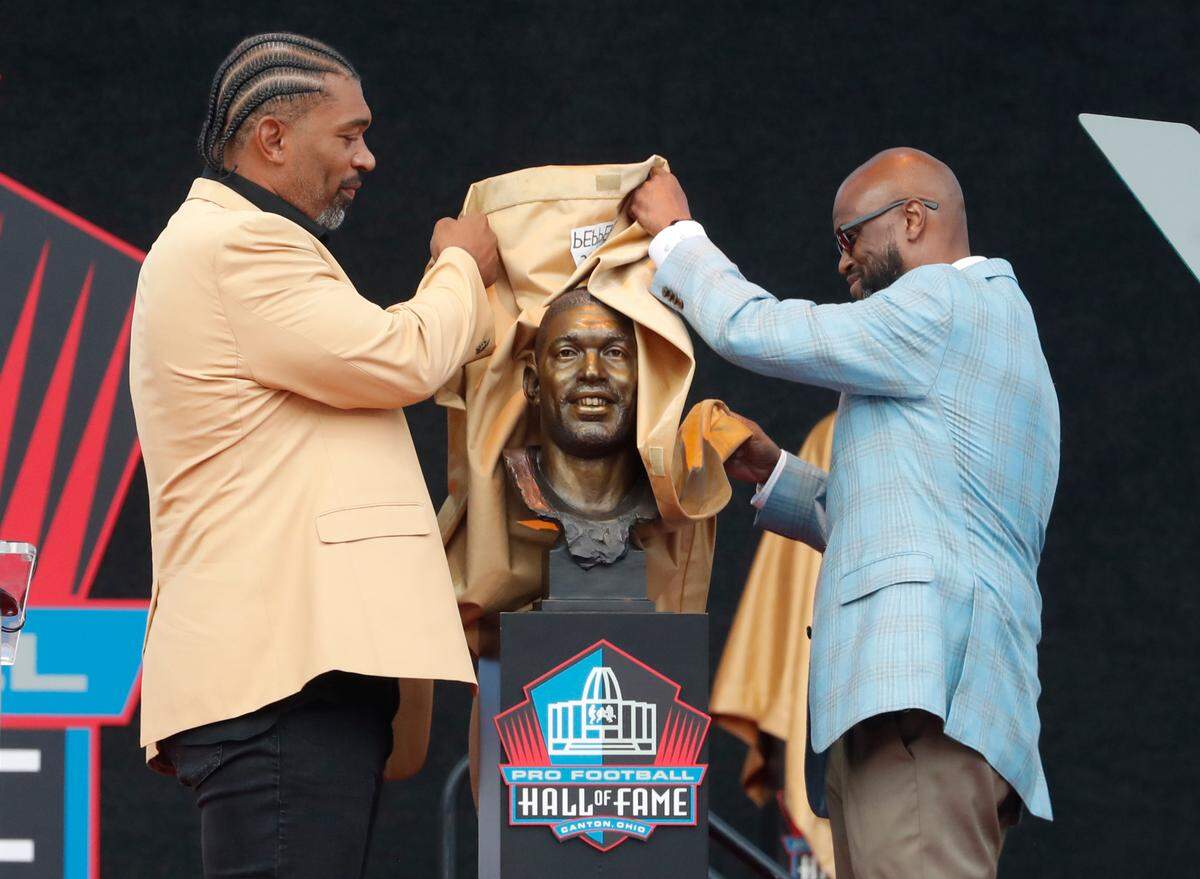 Aug 3, 2024; Canton, OH, USA; Julius Peppers (left) and his presenter Carl Carey (right) unveil the bust of Peppers as he is inducted into the Pro Football Hall of Fame at the enshrinement ceremony at Tom Benson Hall of Fame Stadium. Mandatory Credit: Charles LeClaire-USA TODAY Sports