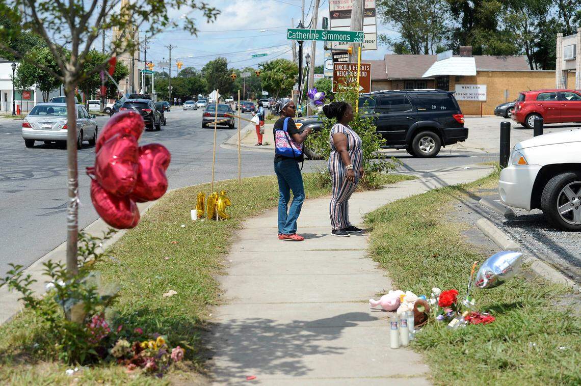 Pedestrians look at memorials set up near the corner of Beatties Ford Road and Catherine Simmons Avenue on Tuesday, June 23, 2020, in memory of three people killed at an outdoor party on Sunday night.